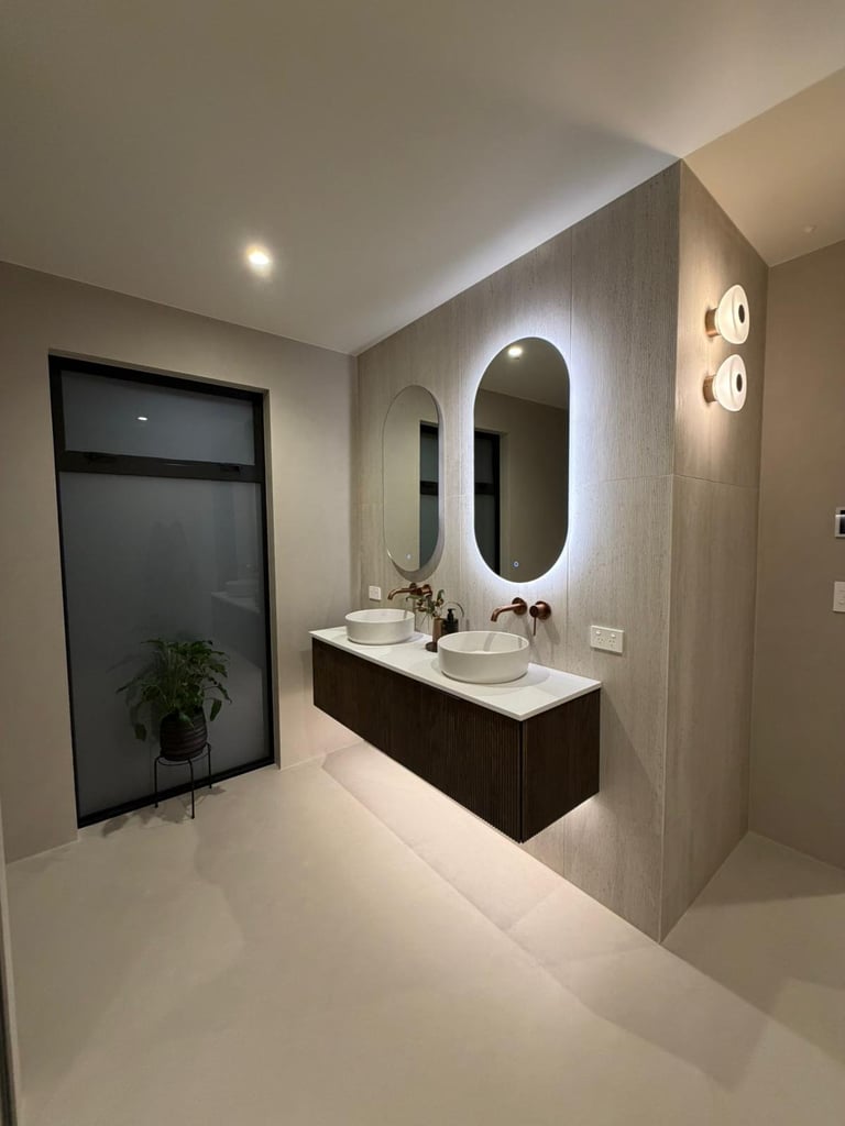 Modern bathroom with double sink vanity, oval mirrors, dark cabinetry, and neutral tile walls