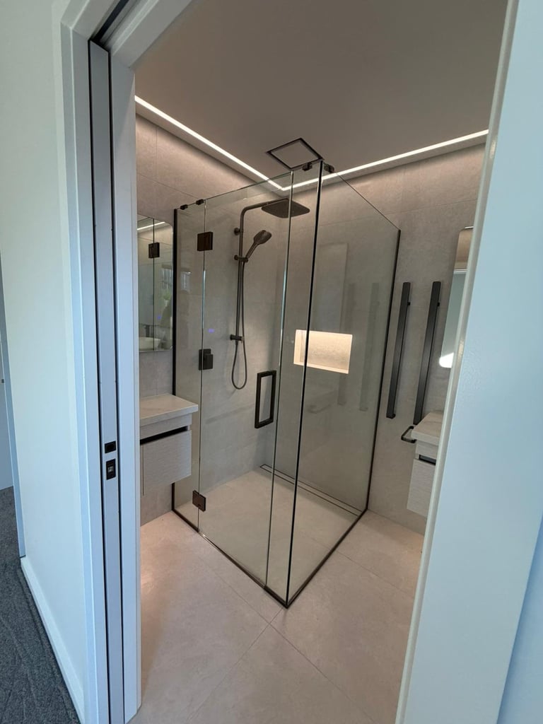 Modern frameless glass shower enclosure with black metal fixtures and rainfall showerhead in a contemporary bathroom