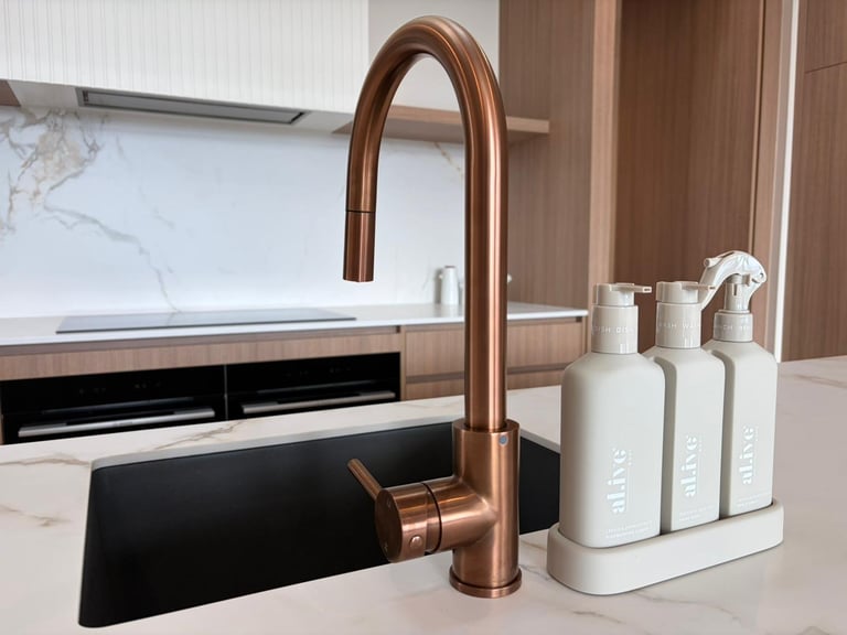 Modern kitchen sink with copper-bronze faucet and white soap dispensers on countertop near stove and marble backsplash