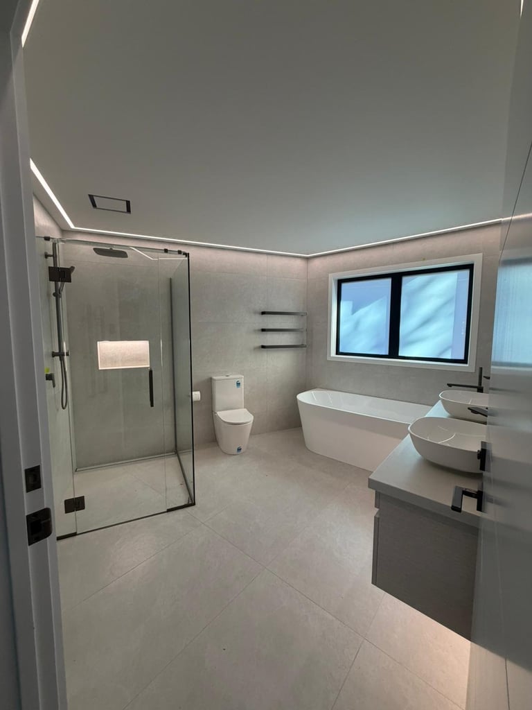 Modern bathroom with glass shower enclosure, dual sinks, freestanding tub, and LED ceiling lights